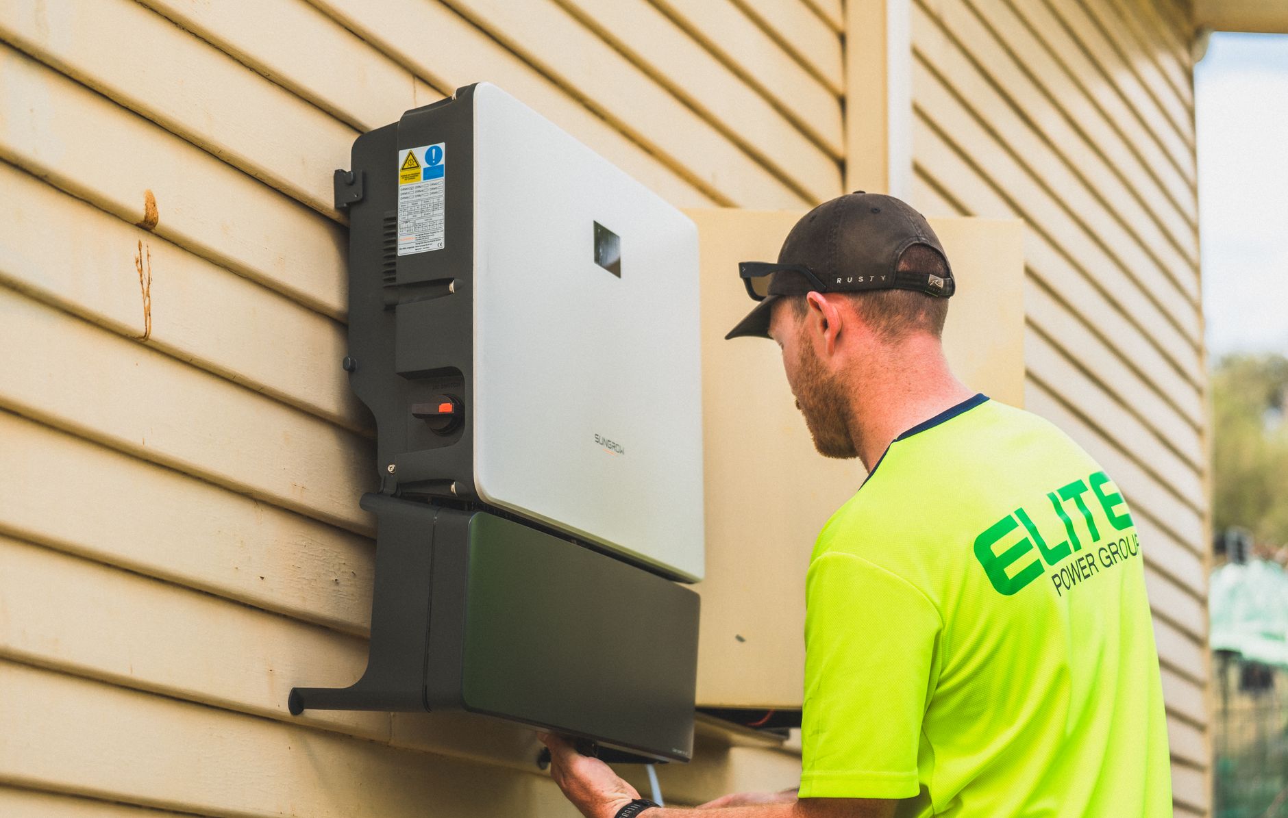 A wall-mounted home battery backup system installed on a garage wall with a white inverter and cables